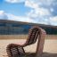 Sofa Wave, moderna panca da esterno in legno su superficie sabbiosa in ambiente urbano.