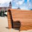 Panca in legno Sofa Wave su una spiaggia sabbiosa con un edificio sullo sfondo.