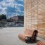 Panchine in legno da esterno Sofa Wave vicino a un edificio moderno con pareti in mattoni.