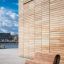 Moderno Sofa Wave in legno posizionato davanti a un edificio contemporaneo.