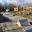 Skate park con rampe accanto a un'area giochi e edifici sullo sfondo.