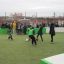 Bambini che giocano a calcio in Multiarena con spettatori sullo sfondo.