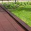 Rubber Tiles 55 pavimentazione di sicurezza per parco giochi in rosso scuro accanto a erba e piante verdi