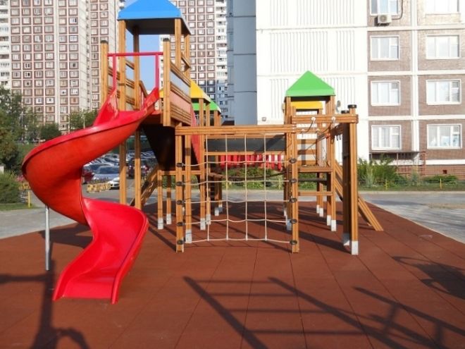 Area giochi per bambini con strutture in legno e scivolo rosso su Rubber Tiles 75.