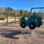 Gioco a dondolo verde Double Auto in un parco giochi con una struttura in legno e altalene sullo sfondo