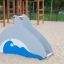 Scivolo da parco giochi Dolphin Slide a forma di delfino in un parco giochi sabbioso.