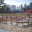 Struttura da parco giochi all'aperto 'Poison Ground' con elementi di arrampicata in legno e uno scivolo rosso su una sabbia