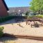 Area giochi naturale 'Poison Ground' con strutture in legno e sabbia in un quartiere residenziale.