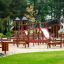 Parco giochi in legno Poison Ground con scivoli e strutture da arrampicata in un parco.