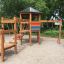 Set da parco giochi in legno Six Angle with Suspension Bridge single slide in un'area giochi sabbiosa.