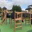 Parco giochi Explorer castle with slide in legno e pannelli neri su superficie verde.
