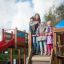 Bambini che giocano su una grande struttura da parco giochi in legno con uno scivolo.