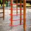 Activity Center with Slide in legno con barre rosse per arrampicarsi in un parco giochi sabbioso.