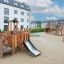 Rubik Modern Nature wooden playhouse with slide su un parco giochi sabbioso con edifici residenziali in th