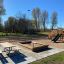 Parco giochi in legno con altalene, scivolo e sabbiera in un parco.
