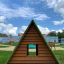 Struttura da gioco in legno Small House Grass Roof con tetto verde in un contesto di parco.