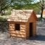 Struttura in legno Nature Playhouse in un parco giochi circondato da alberi.