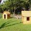 Due strutture in legno Nature Playhouse sull'erba con alberi sullo sfondo.