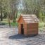 Struttura in legno Nature Playhouse in un parco con un'altalena sullo sfondo.