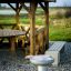 Griglia da esterno accanto a un gazebo in legno con panca e tavolo da picnic.