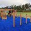 Struttura da parco giochi in legno Somersault Triple su superficie di sicurezza blu in un ambiente esterno.