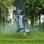 Attrezzatura outdoor Cross Trainer in un parco verde circondato da alberi e prato.