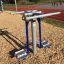 Attrezzatura da esercizio outdoor Double Ski Trainer su terreno di cippato vicino a una pista da corsa.
