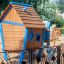 Struttura da gioco in legno Olle's Playhouse con dettagli blu in un parco giochi