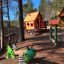 Olle's Playhouse: Casetta da gioco in legno con scivolo e molla verde in un parco giochi a tema foresta.