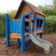 Casetta da gioco in legno Olle's Playhouse con uno scivolo per bambini in un parco.