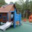 Casetta da gioco in legno con dettagli blu e scivolo in un parco giochi intitolato Olle's Playhouse.